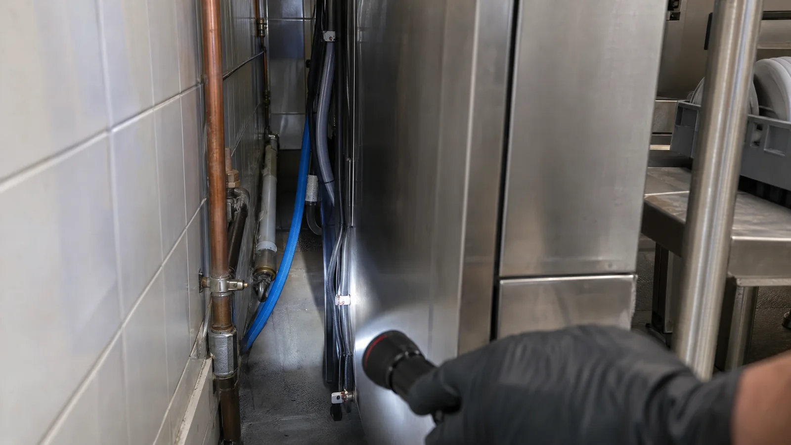 Torch inspection behind a stainless steel commercial dishwasher for a cockroach infestation